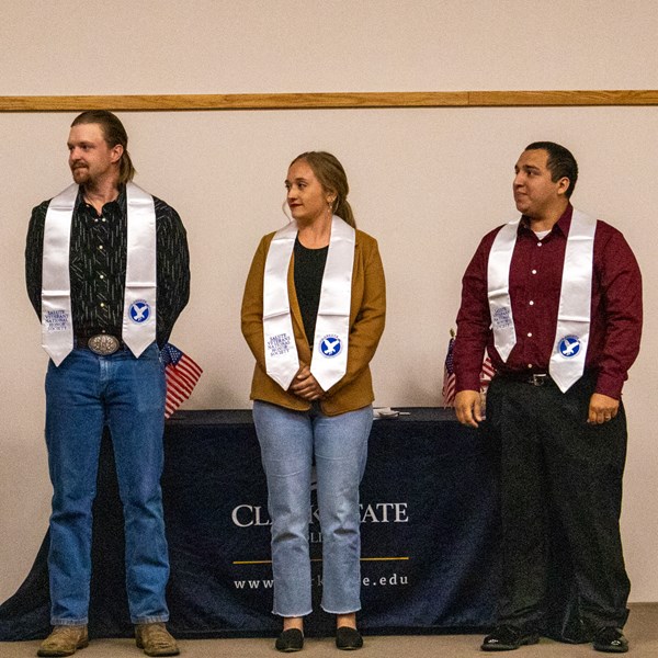 Four individuals at Salute Honor Society induction wearing white draped honorary scarves.