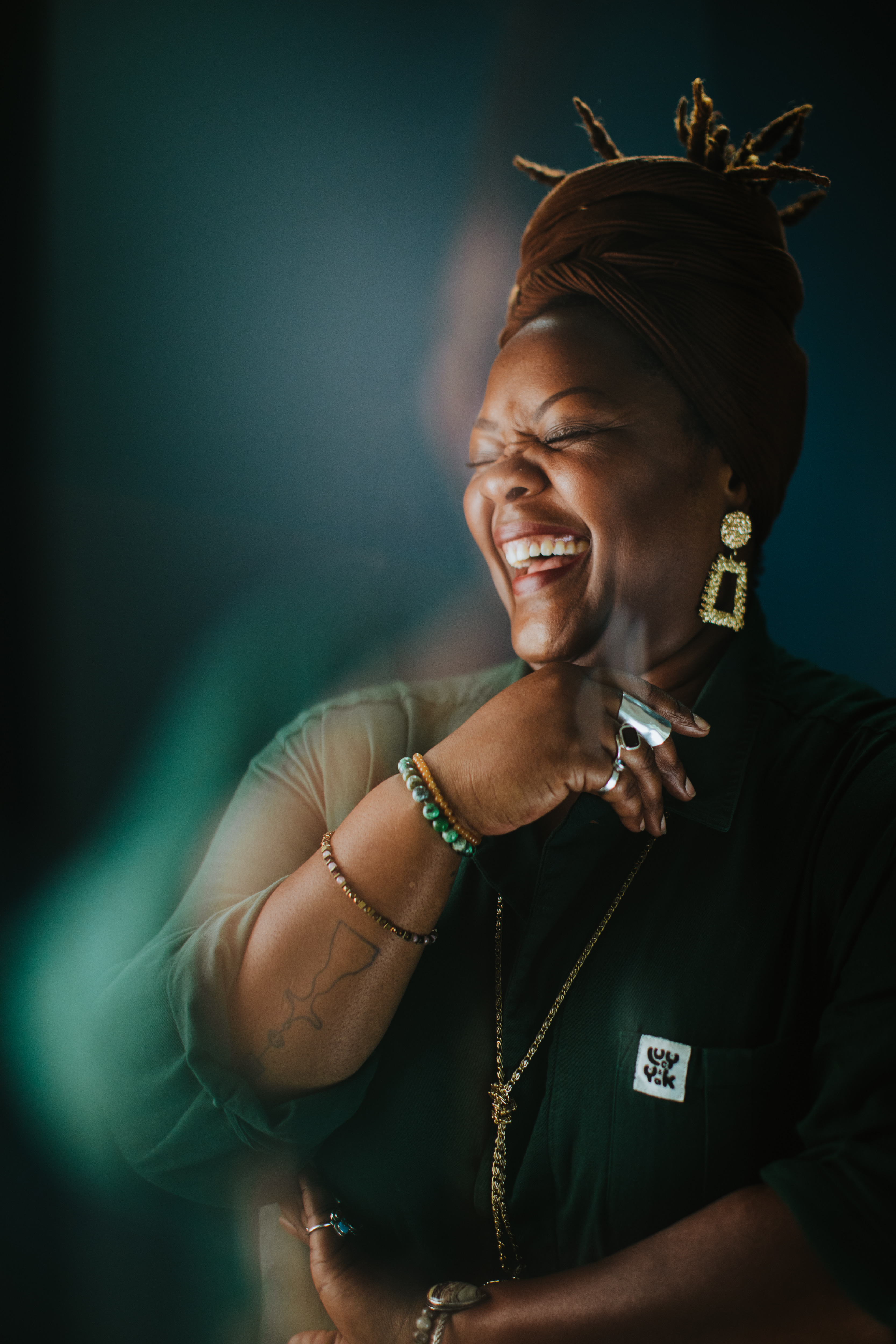 African American woman smiling wearing green flowy dress and gold dangle earrings.