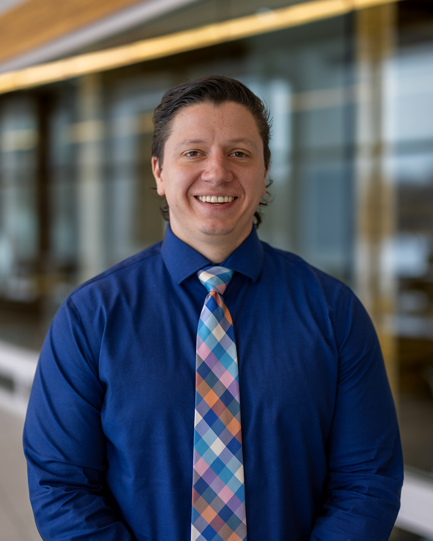 White male wearing blue button down shirt and colorful tie.