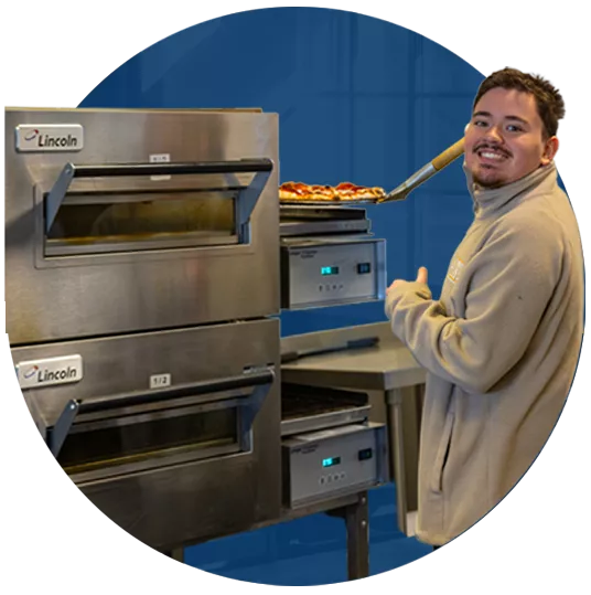 Fresh Abilities employee smiling while pulling pizza out of oven.
