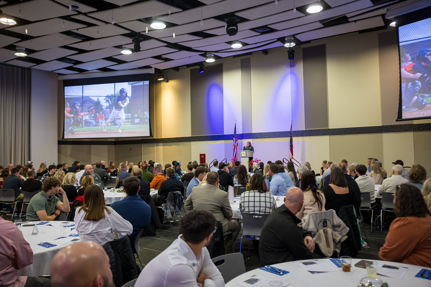 Room full of people sitting at tables looking at a presenter at the podium.
