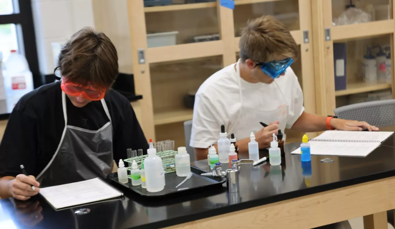 male students in a chemistry lab wearing goggles with chemistry equipment