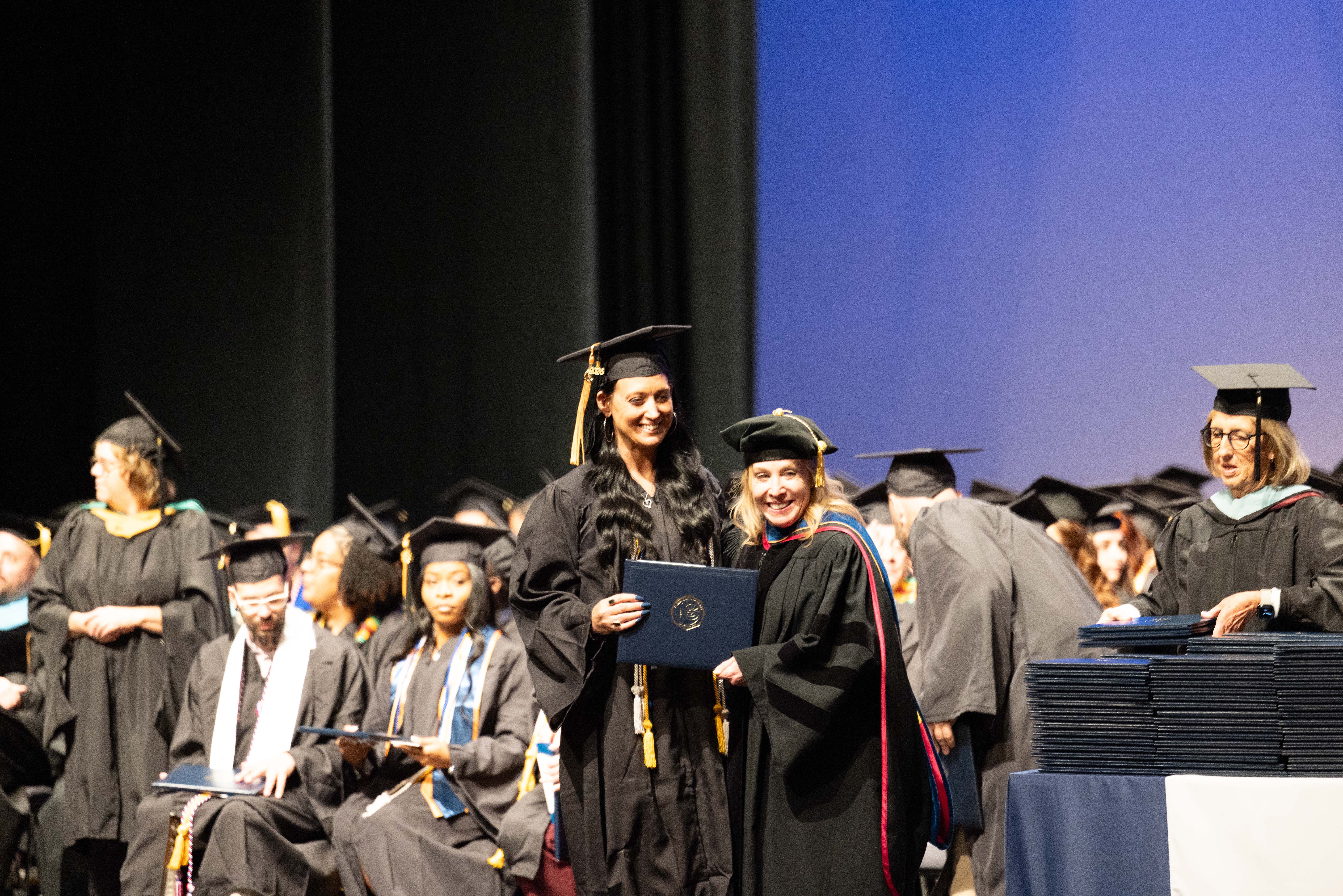 Two women in black graduation robes holding diploma