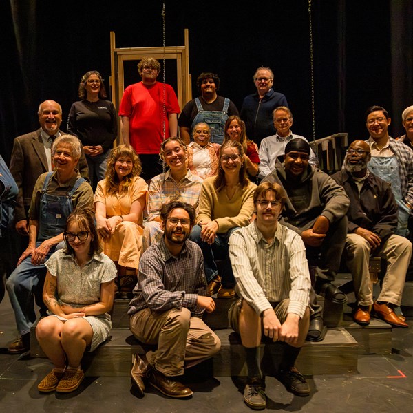 Multiple people sitting and standing on a stage posing for a photo