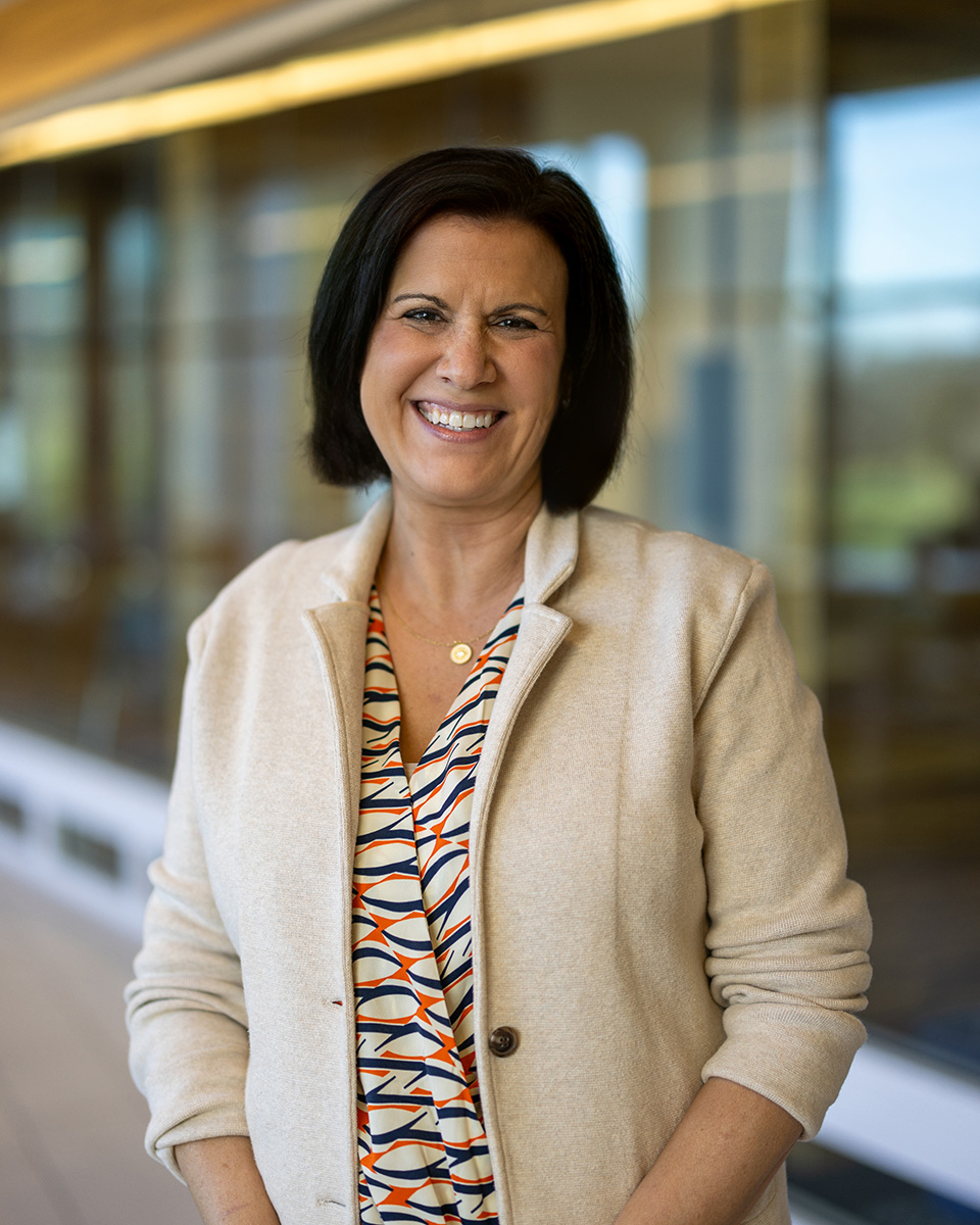 Erika Daggett with orange and blue top and cream cardigan smiling.