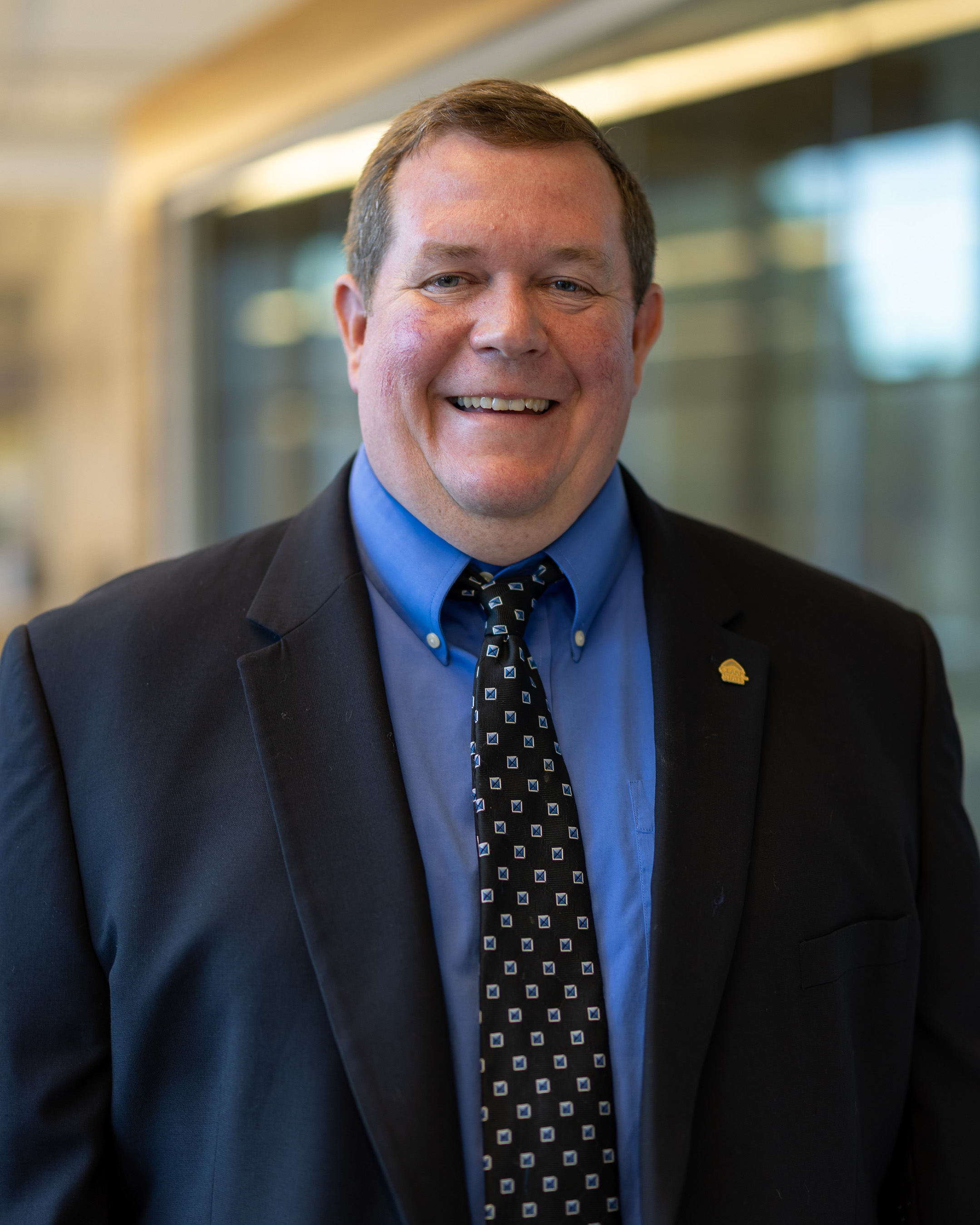 Kyle Hall, a man with short brown hair wearing a black suite and blue dress shirt.