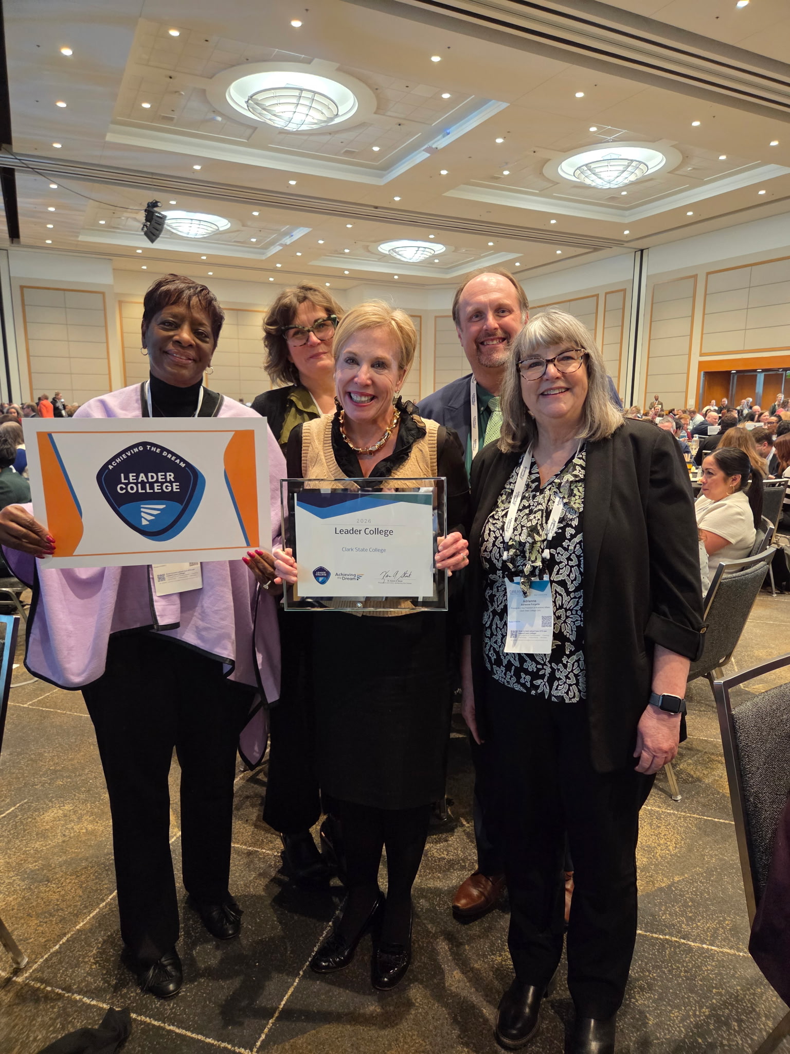 Four smiling women and one man stand holding award 