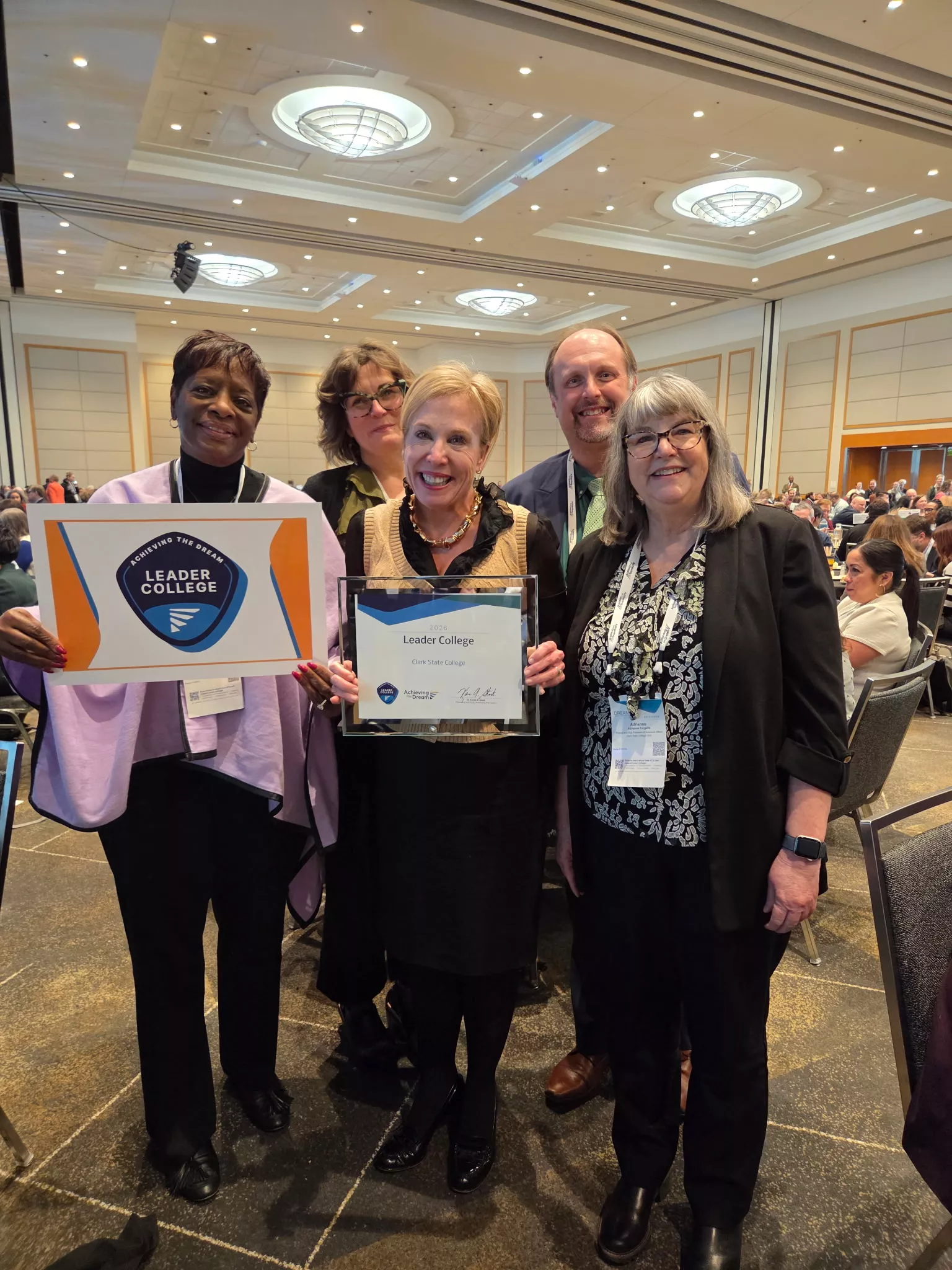 Four smiling women and one man stand holding award 