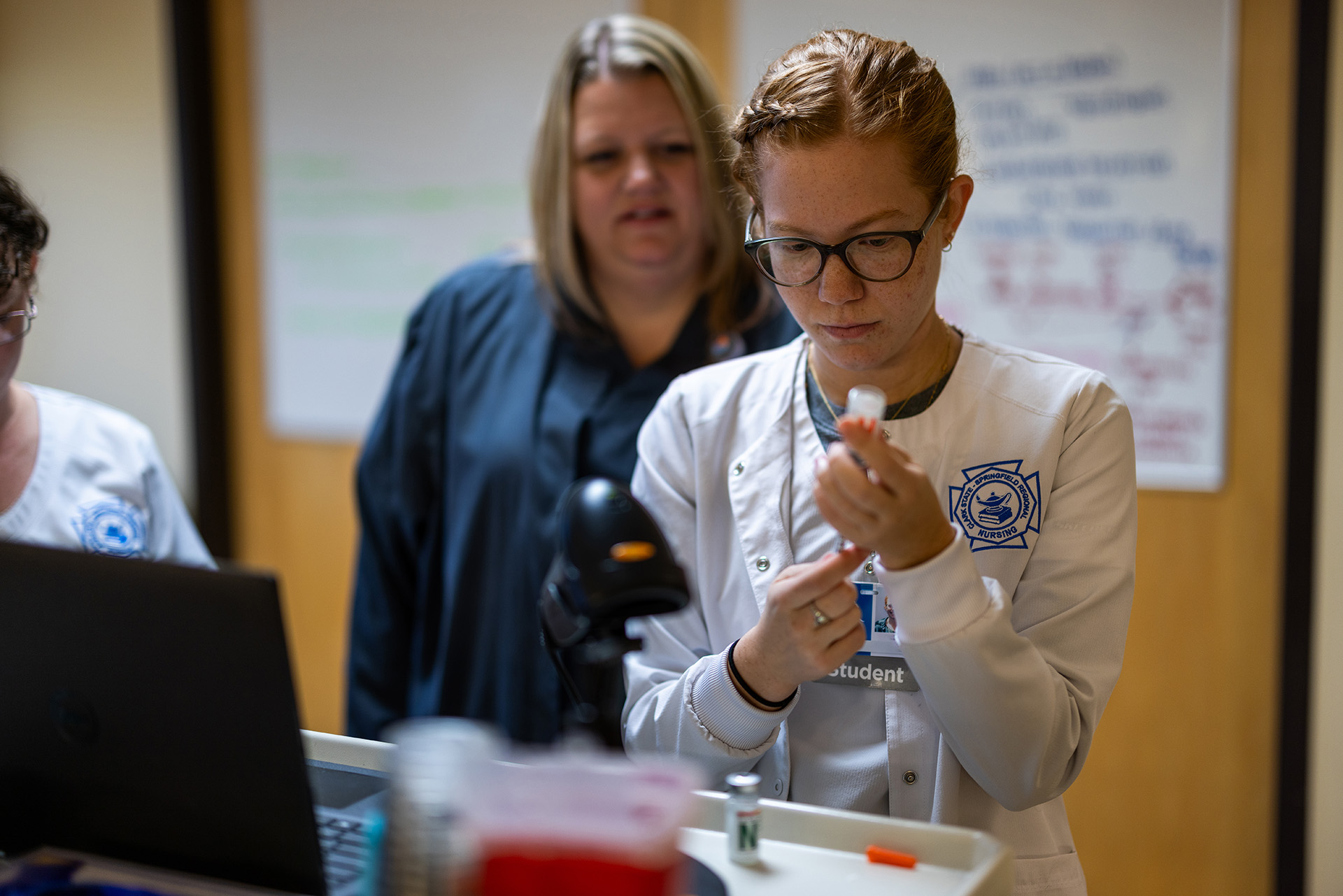 Nursing student wearing white scrubs filling a needle with insulin.