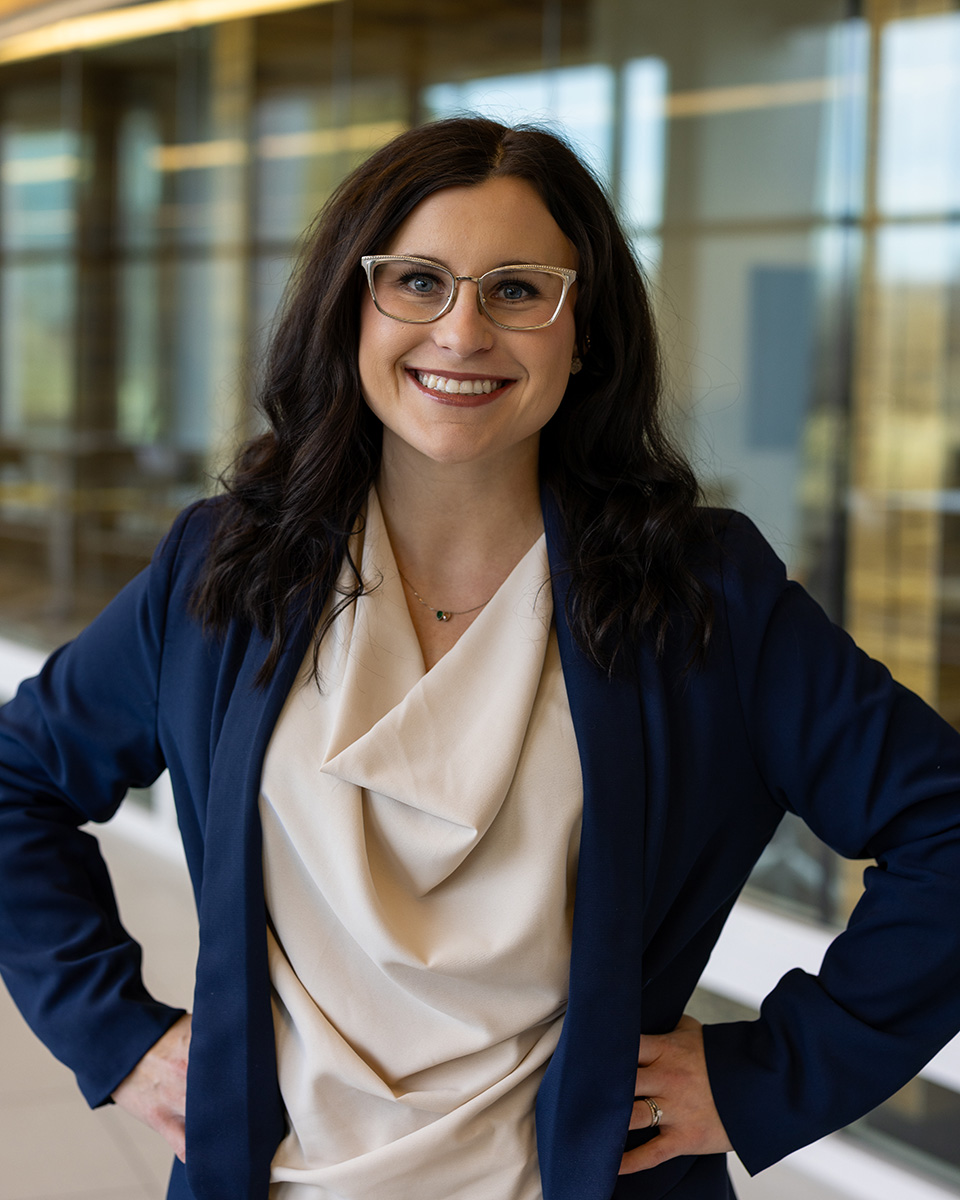 Megan Platfoot wearing a cream top and navy blazer, smiling with her hands on her hips.