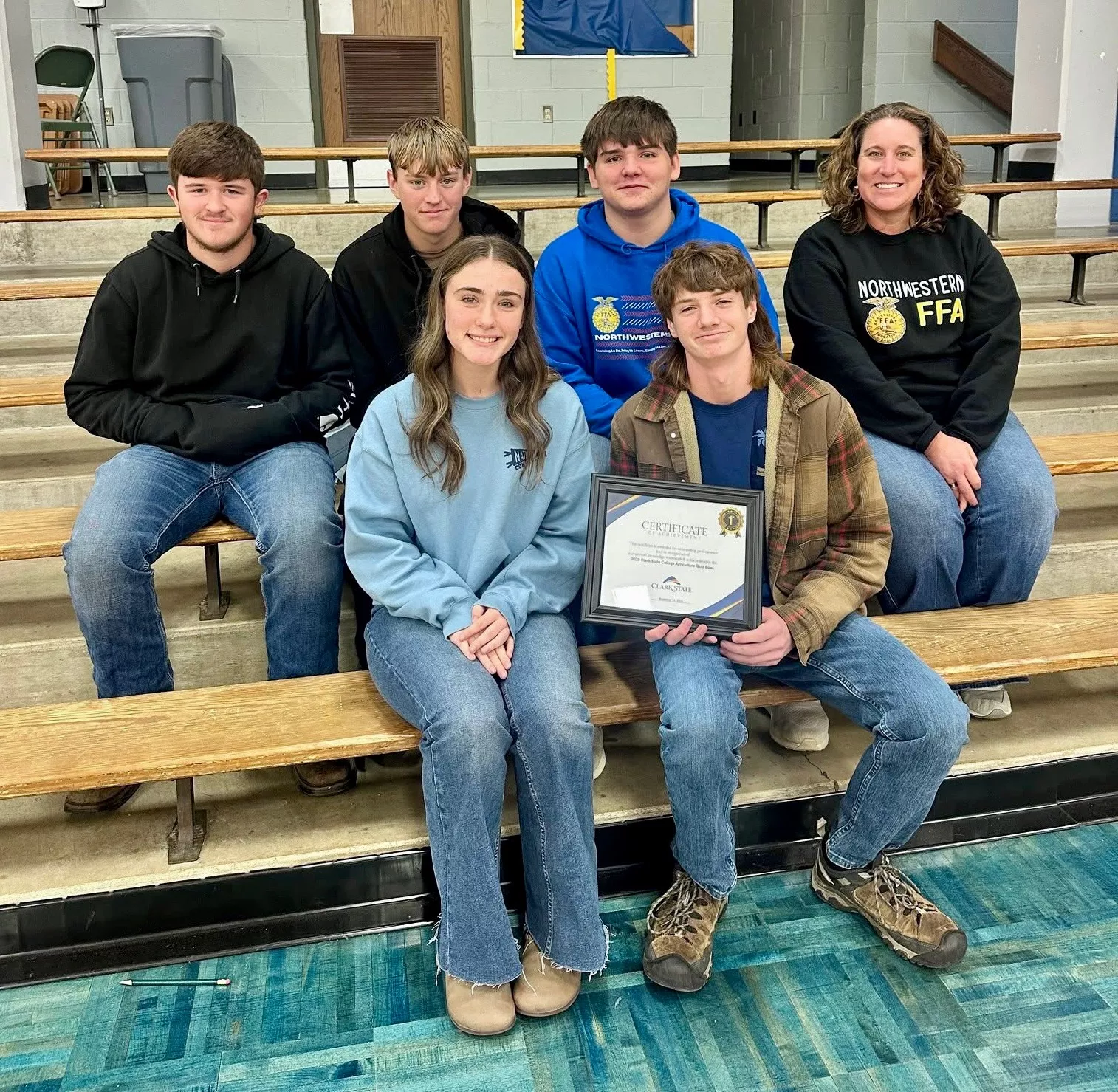 Five students and one teacher sitting in bleachers holding certificate.
