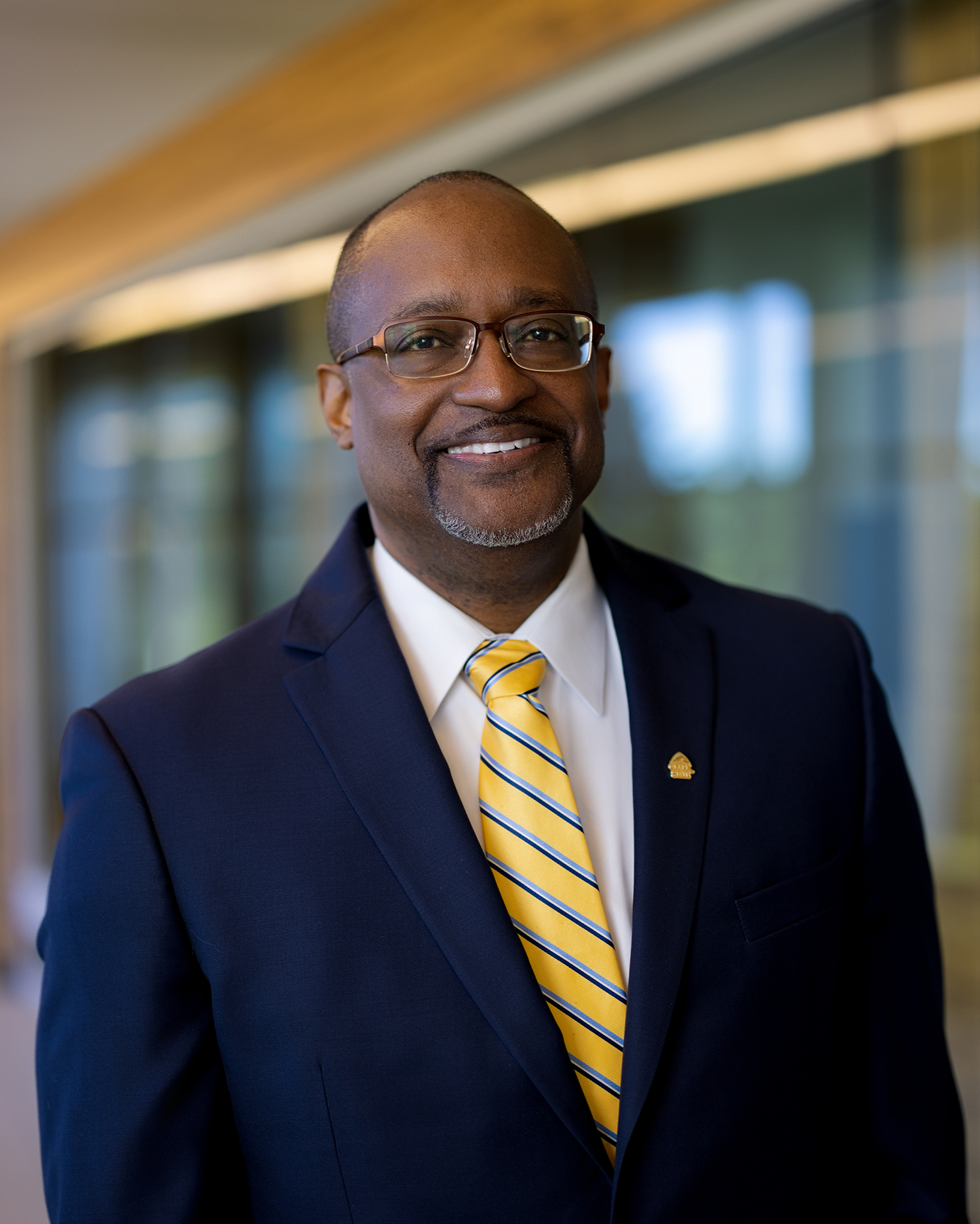 African-American male with navy blue blazer and yellow and blue tie.