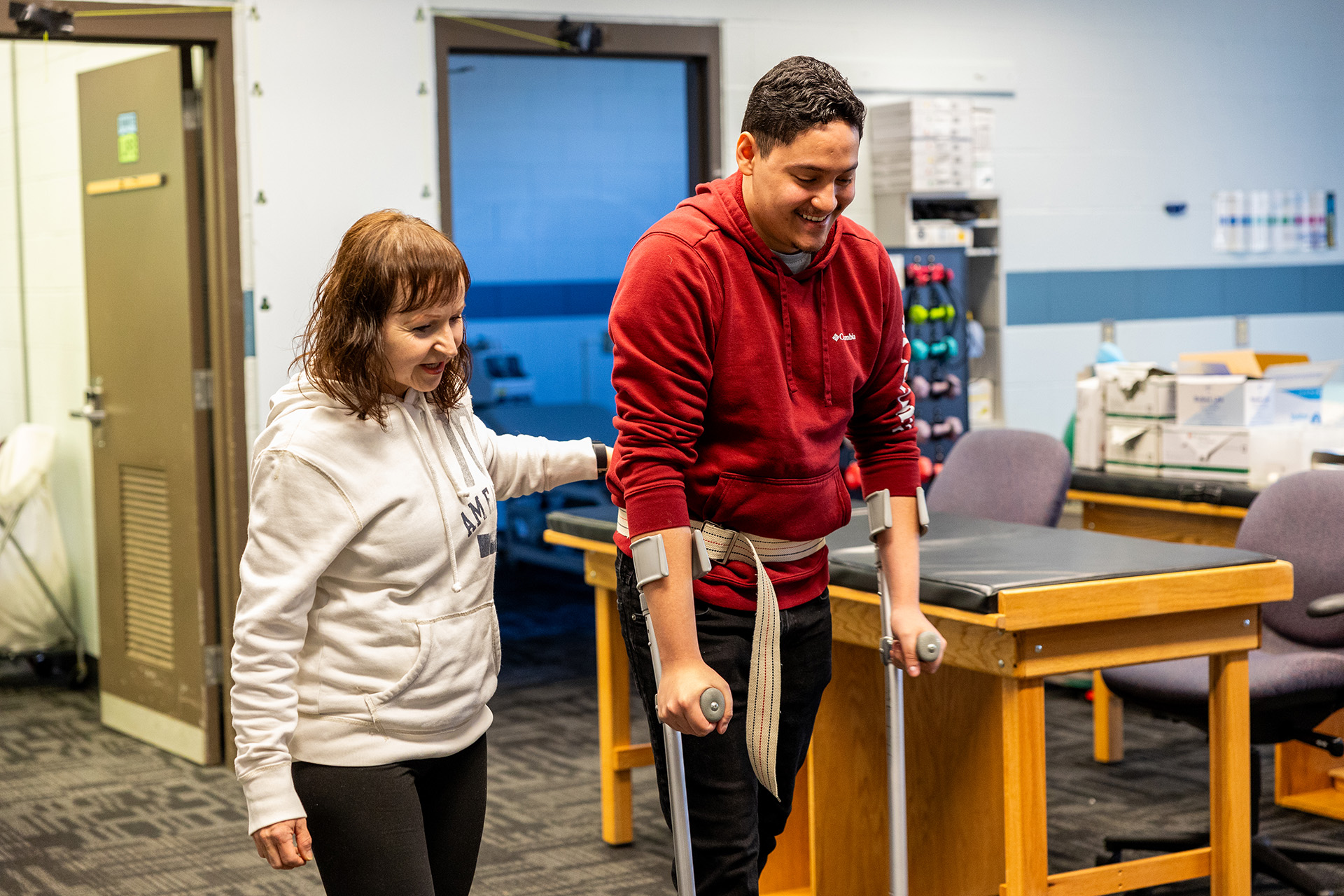 Female student helping a man learn how to walk with crutches.