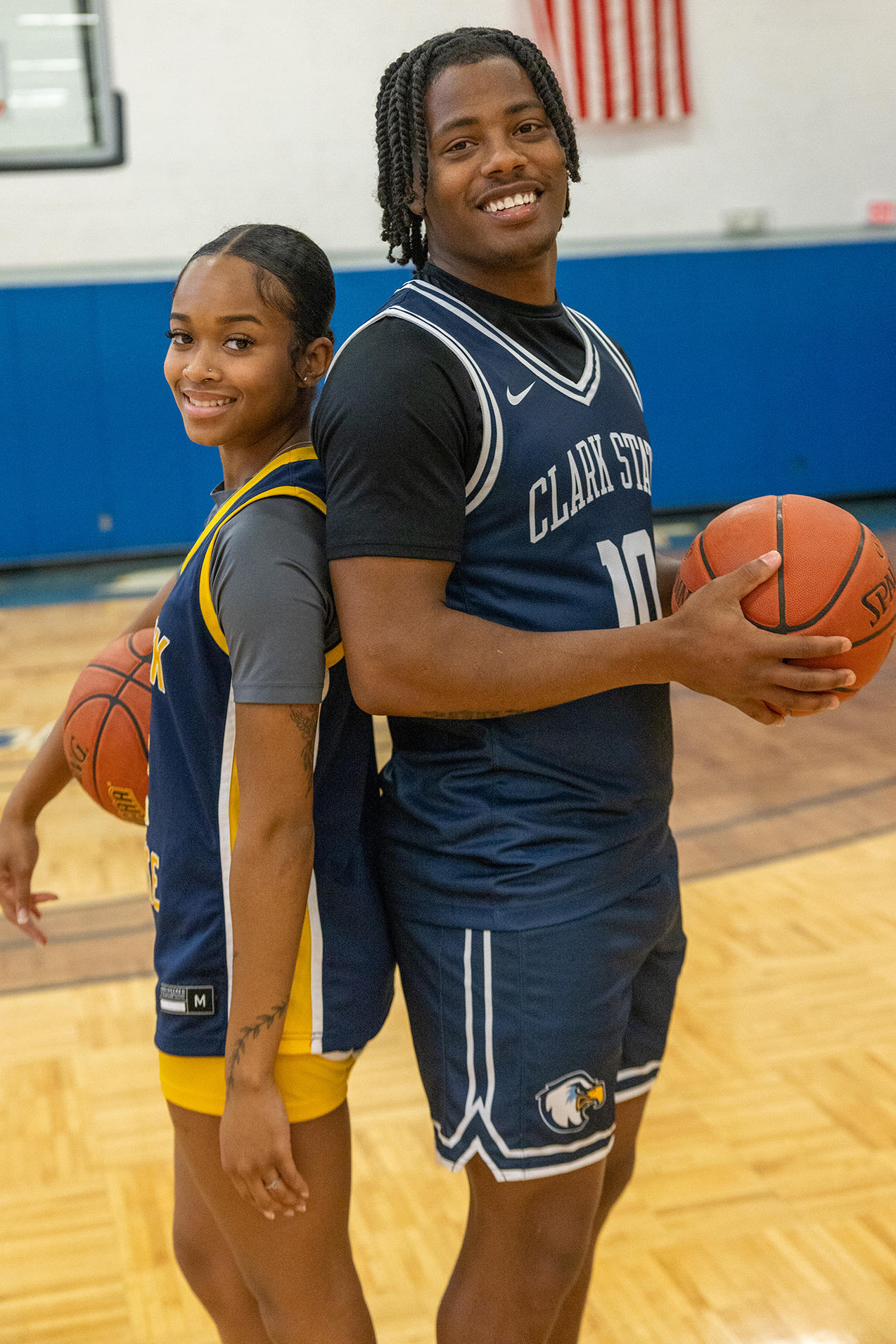 A female and male student wearing Clark State basketball uniforms, holding a basketball in the gym.