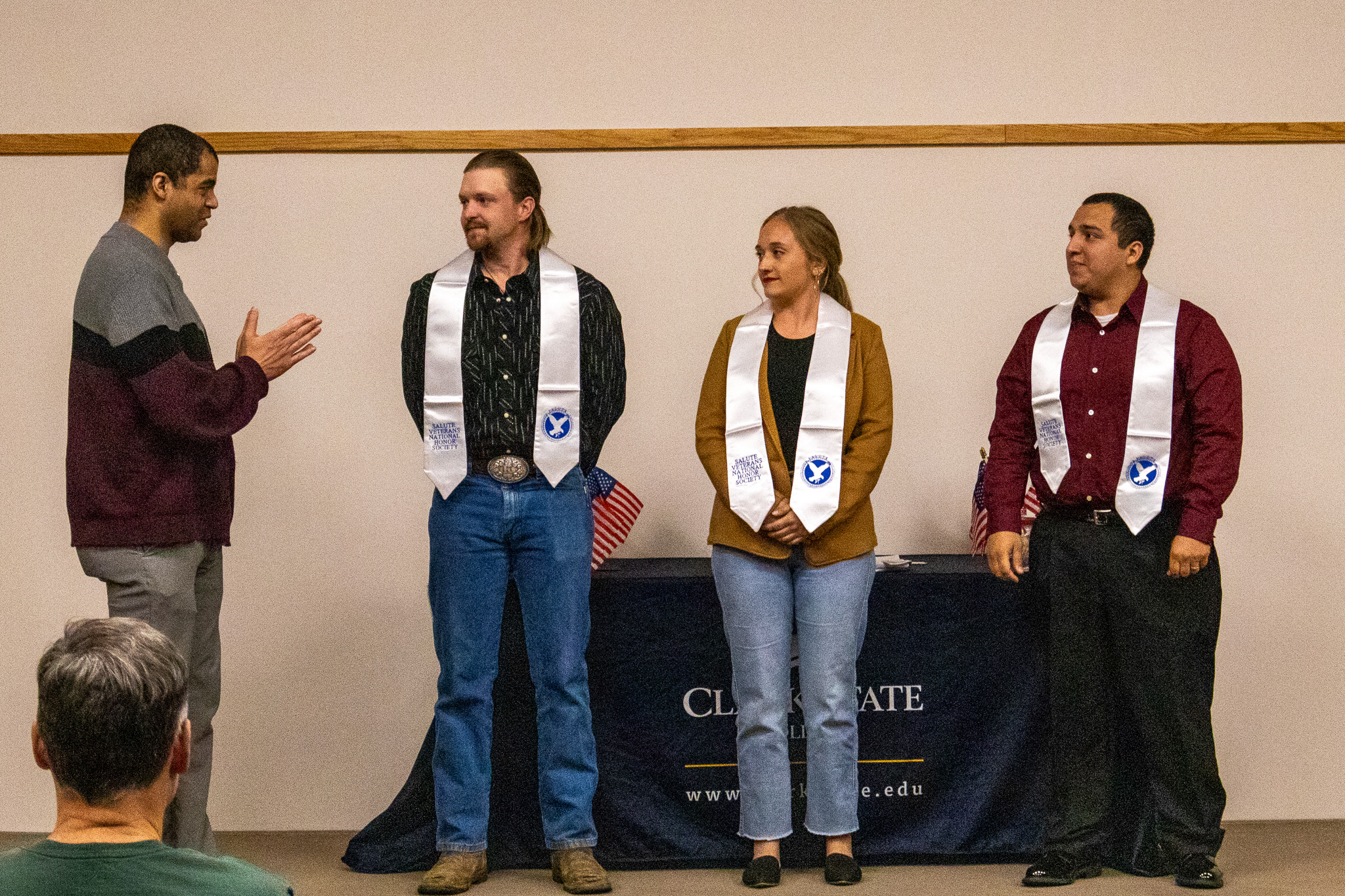 Four individuals at Salute Honor Society induction wearing white draped honorary scarves.