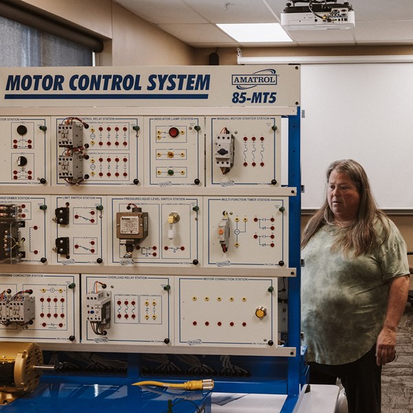 Training board and equipment with knobs, connectors, lights with instructor observing the machine.