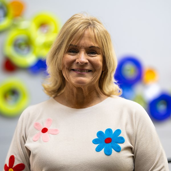 Smiling female with blonde hair wearing white sweater with colorful flowers.
