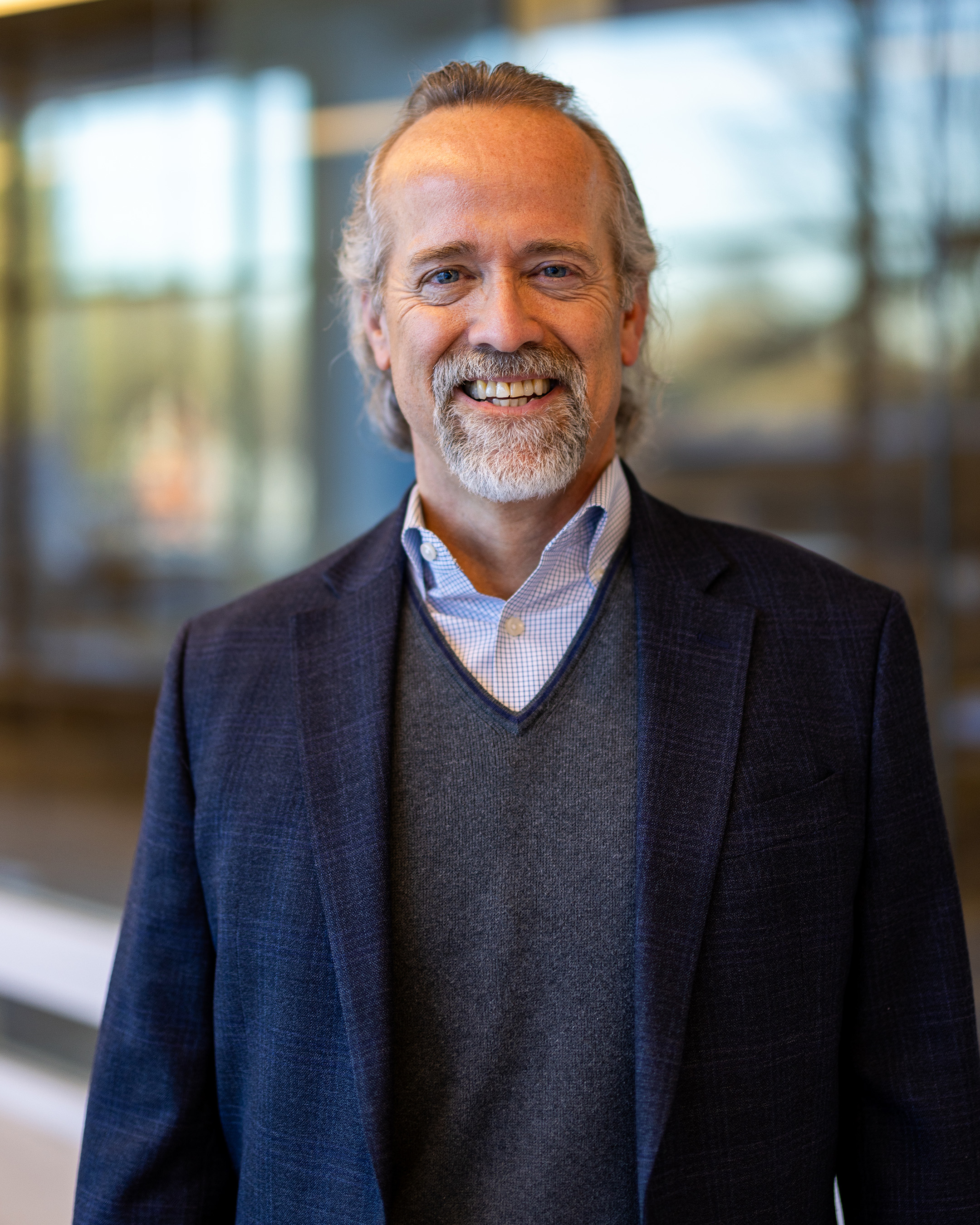 Mitchell Hurst, a man with short grey hair smiling wearing a navy blazer and grey sweater.