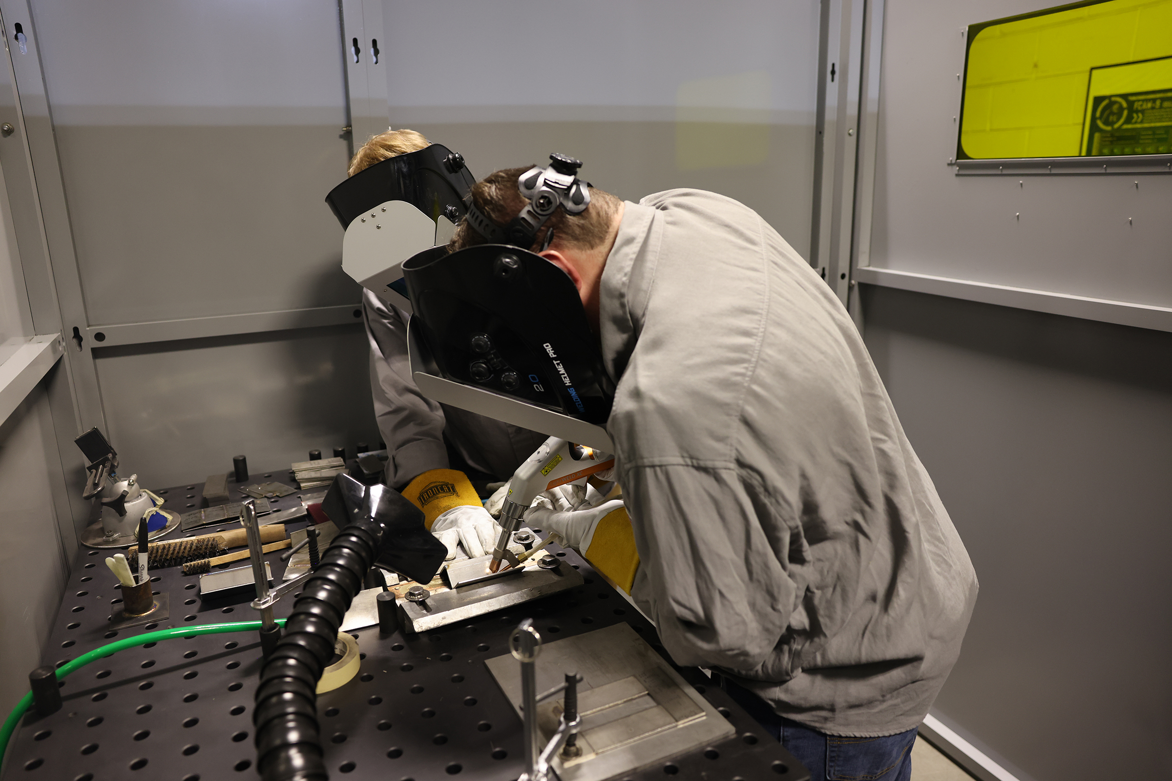 two men wearing welding masks at a table with laser welding machine.