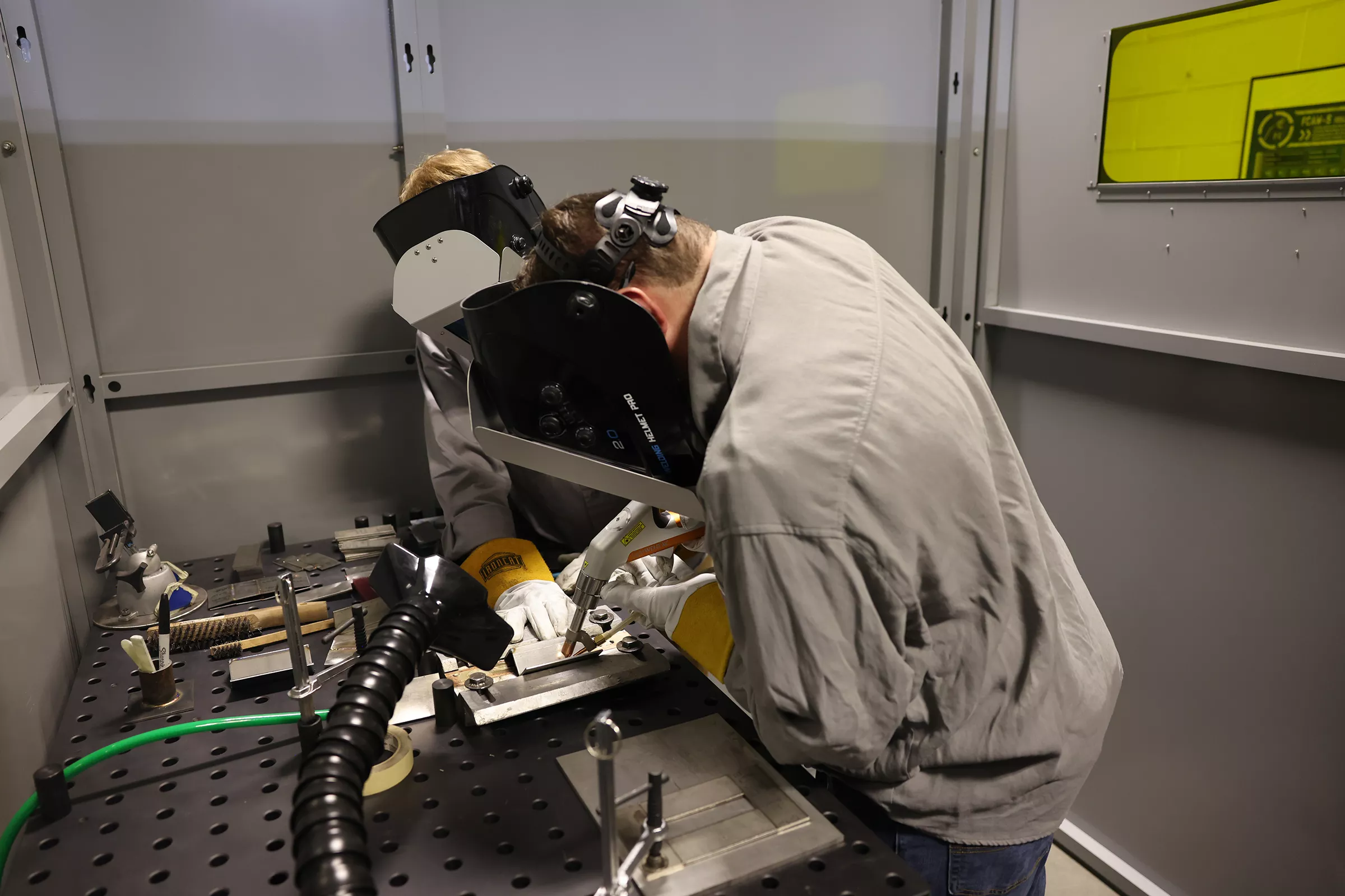 two men wearing welding masks at a table with laser welding machine.
