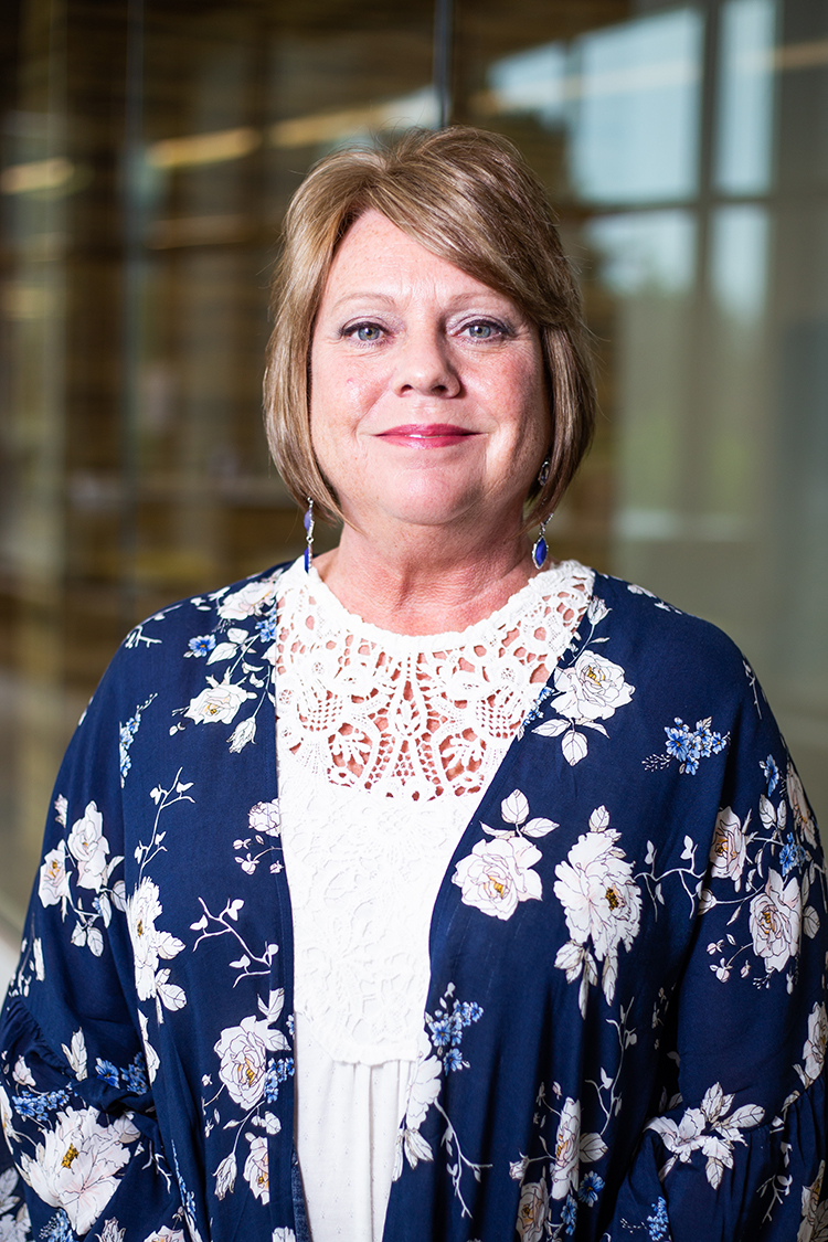  Headshot of a woman with brown hair wearing a navy blue jacket with white flowers.