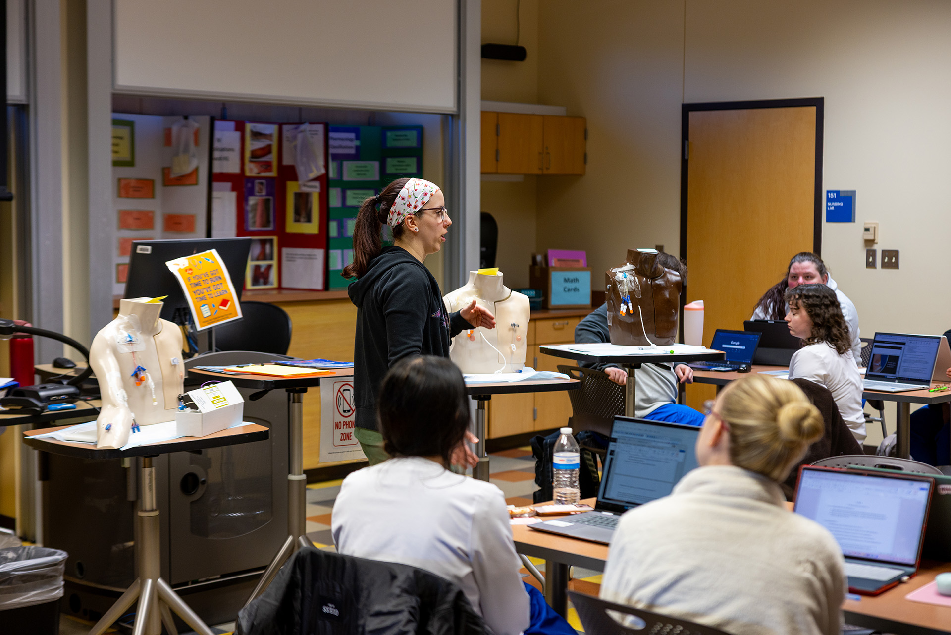 Instructor at the front of classroom guiding students on IV insertion.