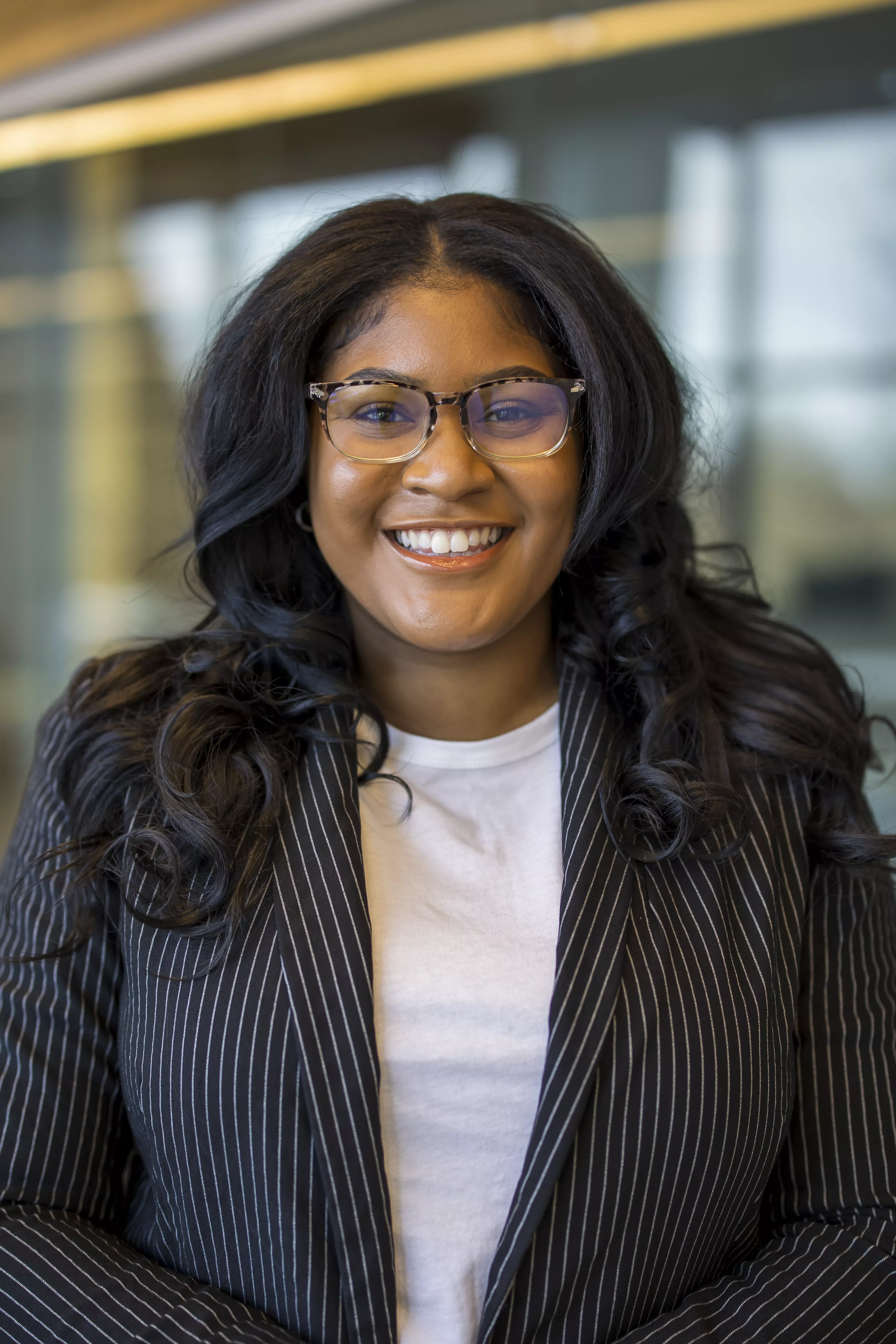 African-American female smiling wearing glasses and a pin striped suit jacket with white shirt.