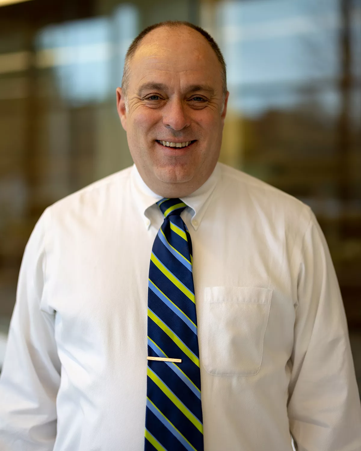 Smiling white male wearing white dress shirt and blue and green striped tie.