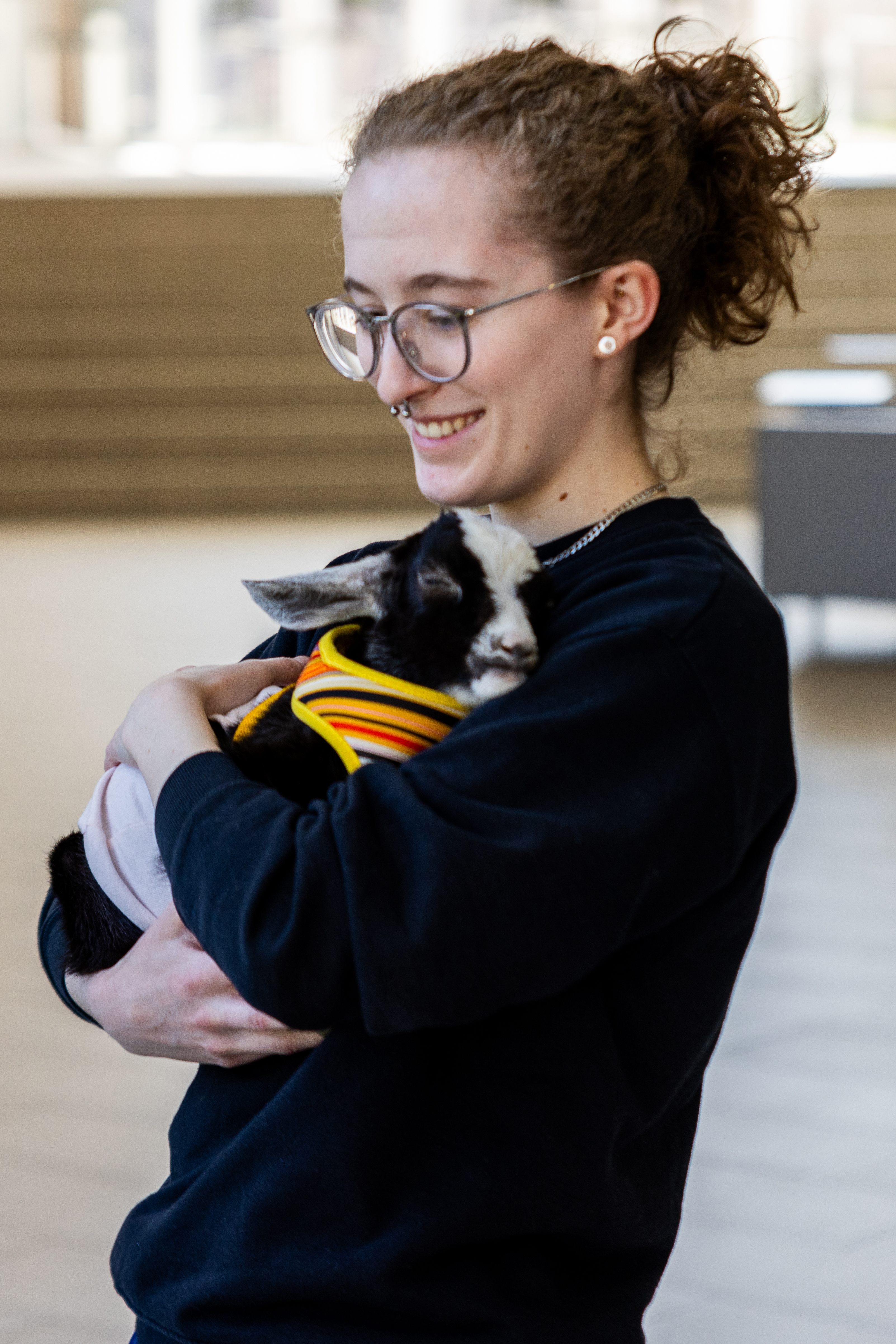 A female student with brown curly hair holds a black and white baby goat.
