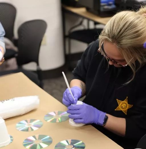 Woman with blonde hair wearing purple gloves collecting fingerprints from a cd.