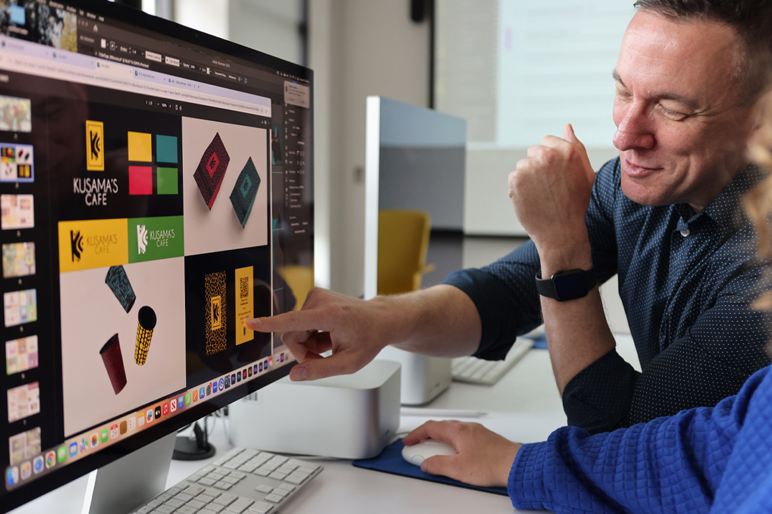 Instructor and student reviewing colorful graphic design layouts on a large computer screen.