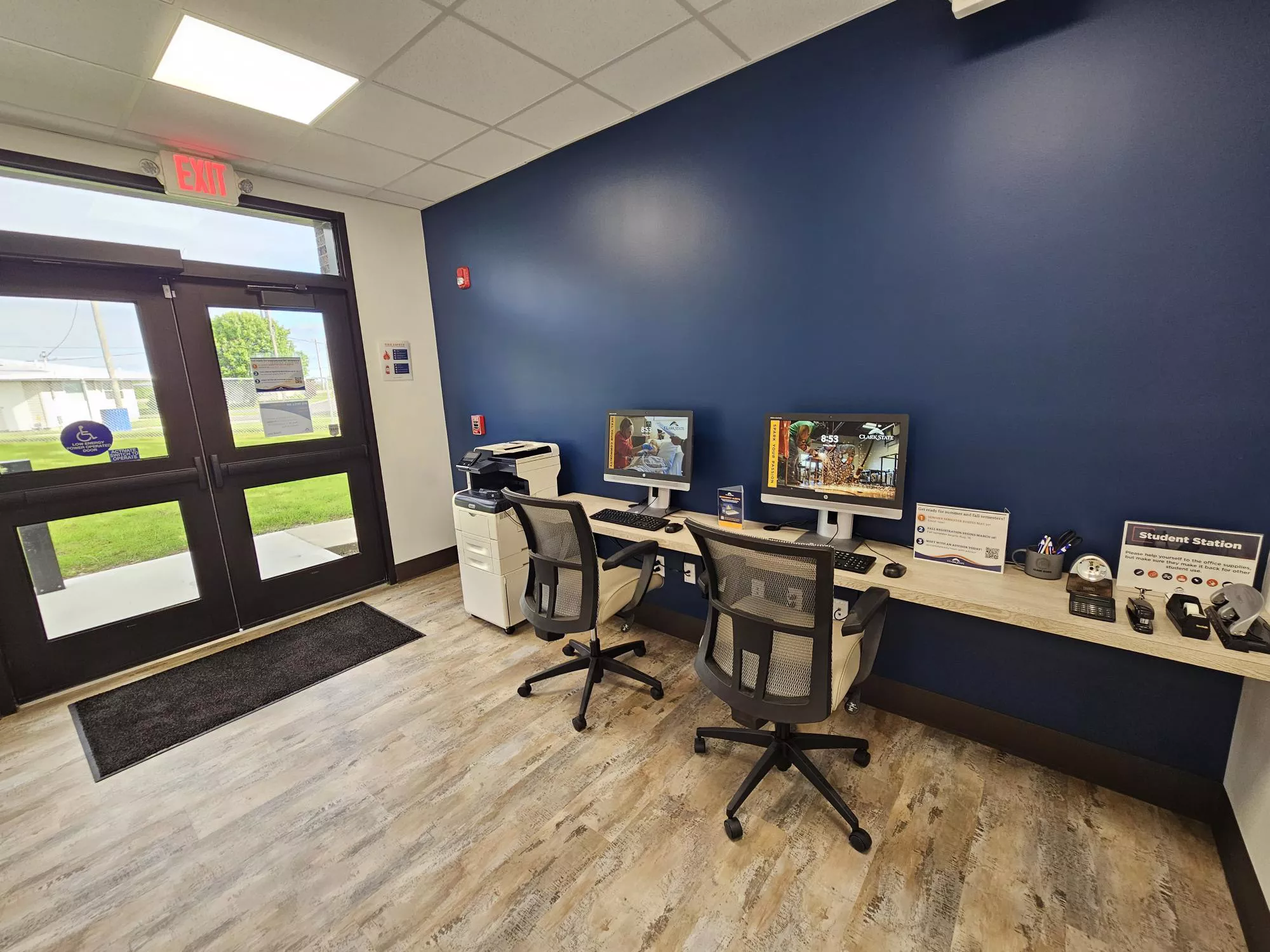 Open area with desk and two computers and chairs, blue wall and glass doors