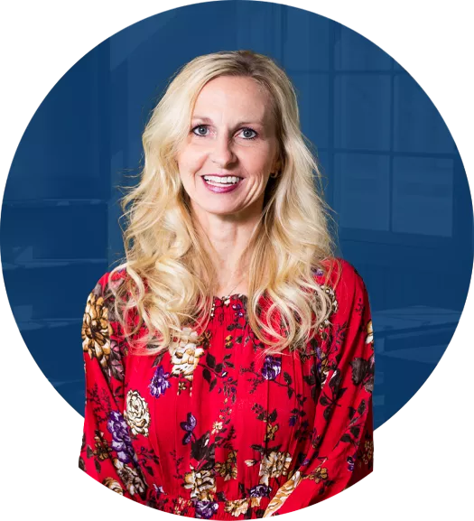 Carol Miller, a women with blonde curly hair smiling wearing a red floral blouse.