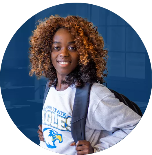 Smiling student wearing a Clark State Eagles sweatshirt and backpack inside a campus building.