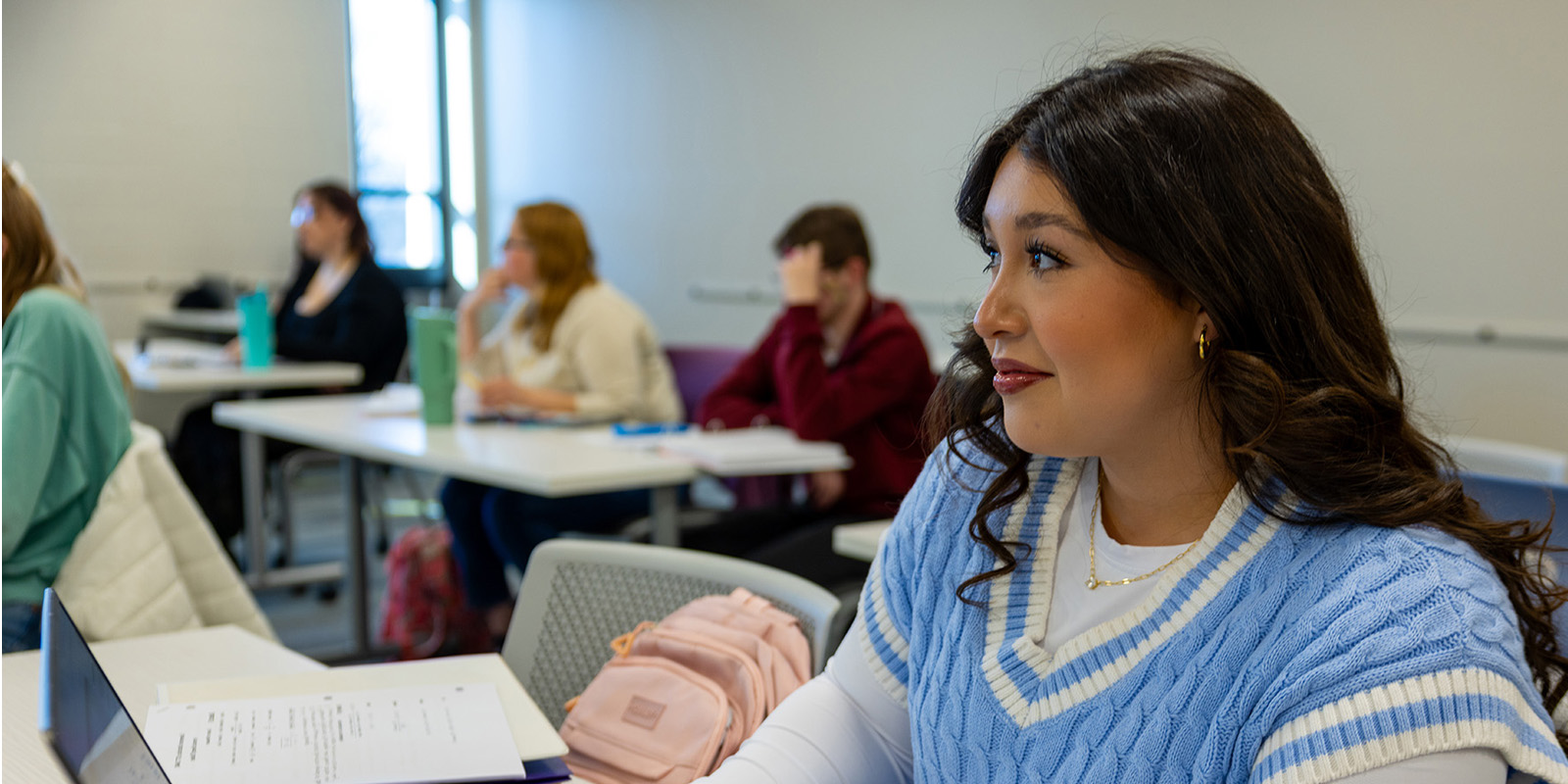 Female student with long curly hair sitting at desk with notes and laptop.