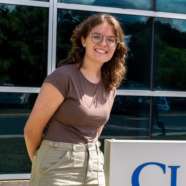 Young woman with brown hair standing next to Clark State sign outside.