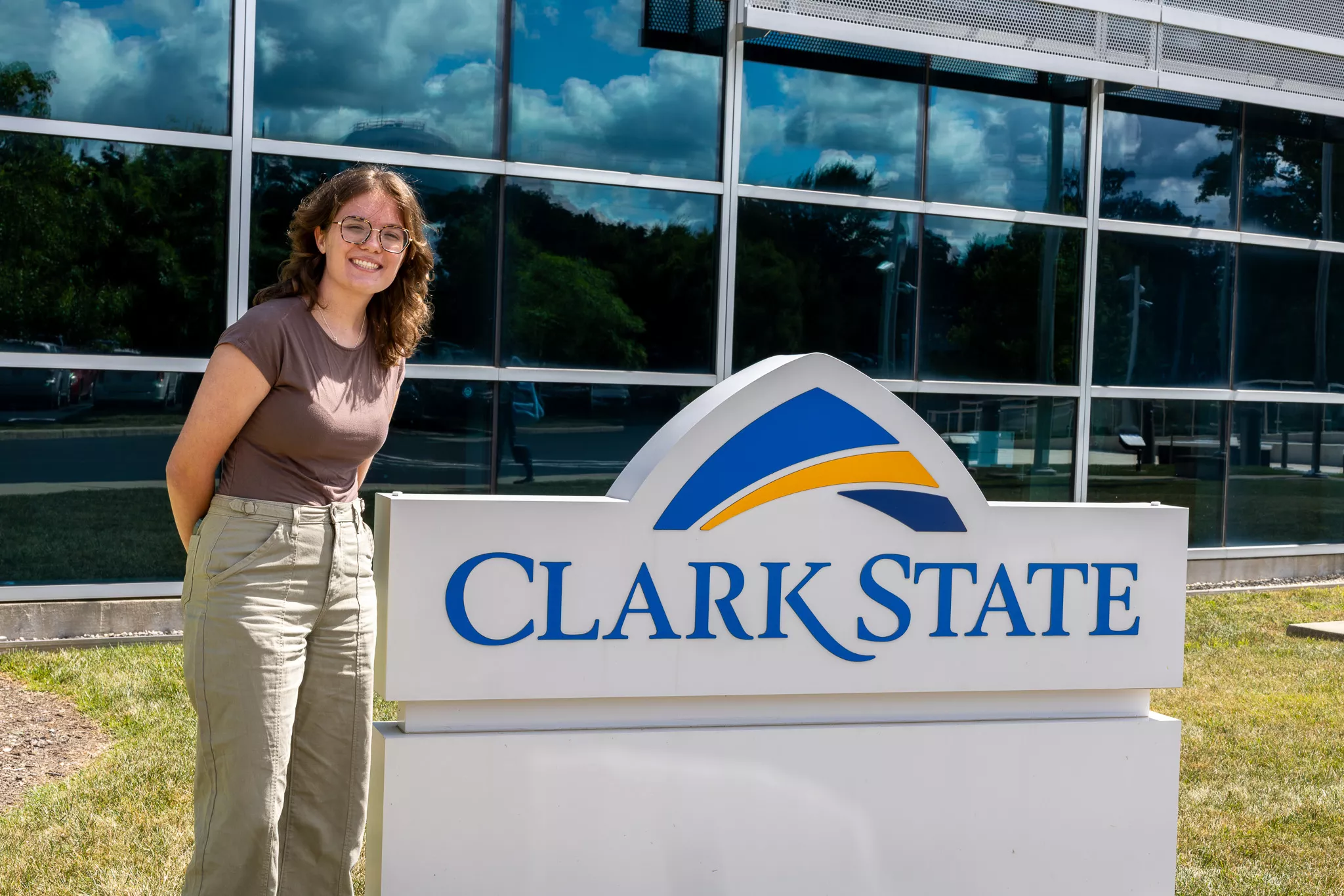 Young woman with brown hair standing next to Clark State sign outside.