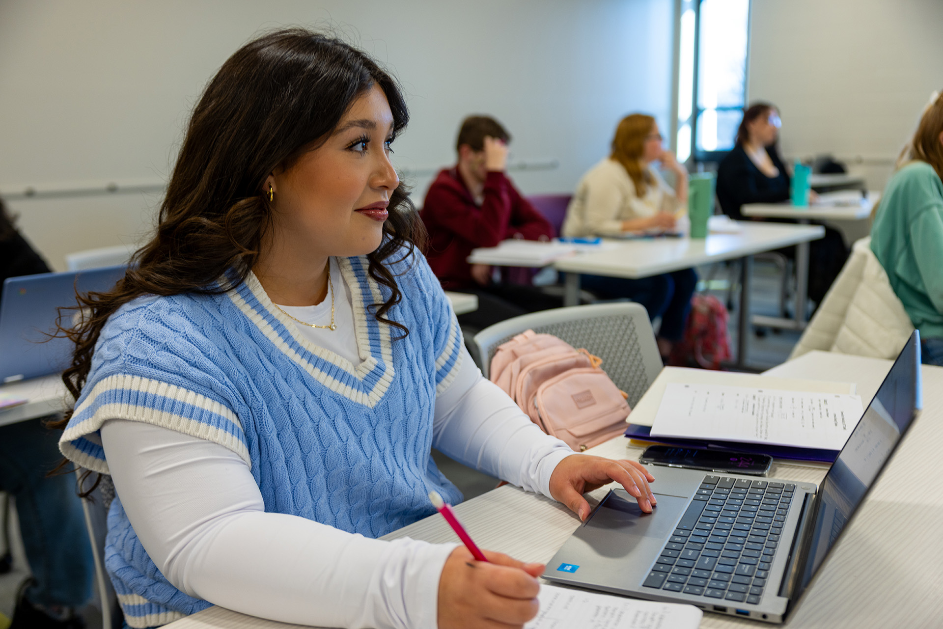 Student wearing a light blue vest working on laptop.
