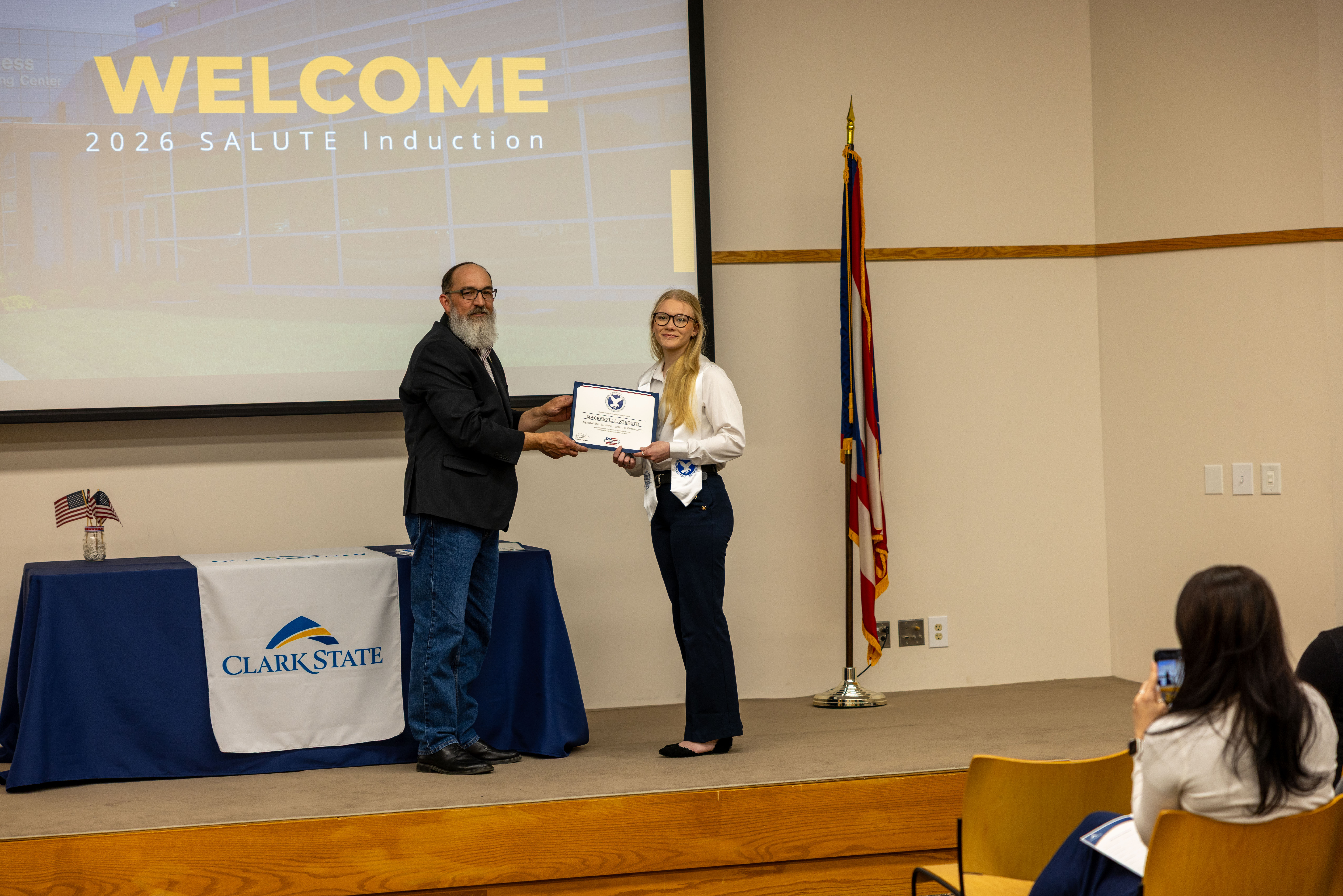 Man hands woman a certificate on a stage.