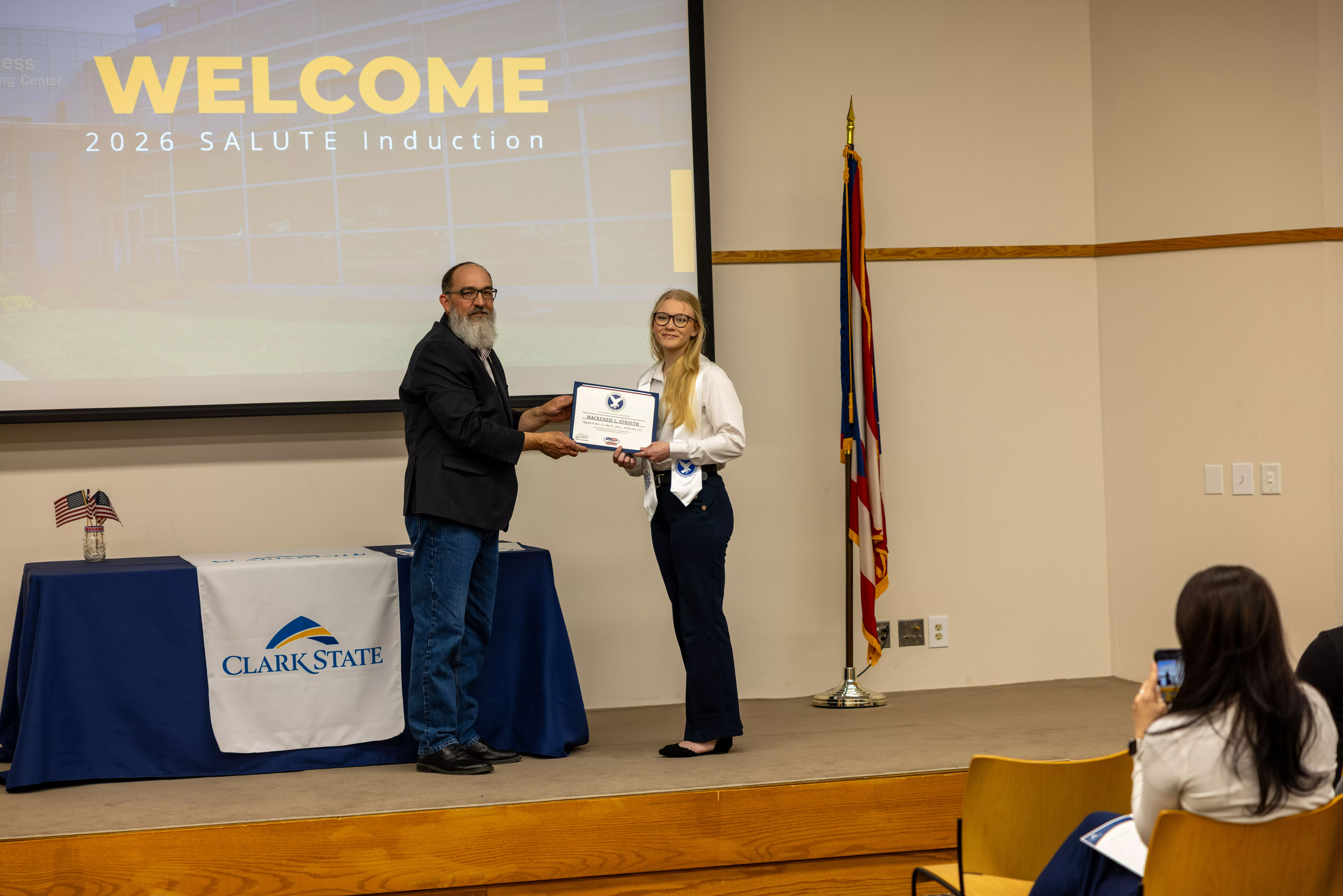 Man hands woman a certificate on a stage.